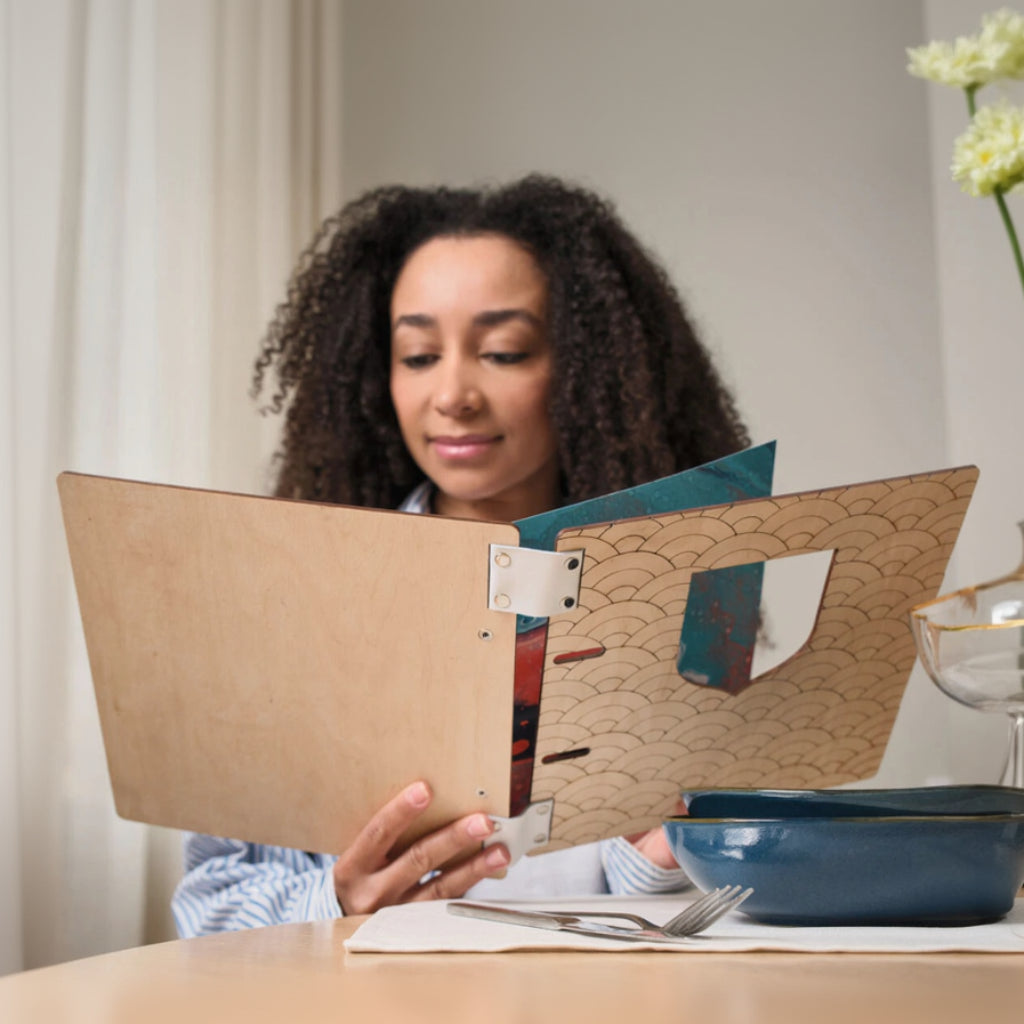 Open light wood menu folder revealing a colorful ocean-inspired painting on the inside cover and chrome ring binder hardware.
