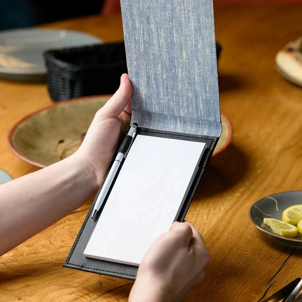 This waiter's notebook boasts a high-quality fabric cover and a solid hardcover, providing a classic and sophisticated look. Ideal for detailed order taking and note-keeping, its strong construction ensures it can handle daily use in demanding restaurant settings.