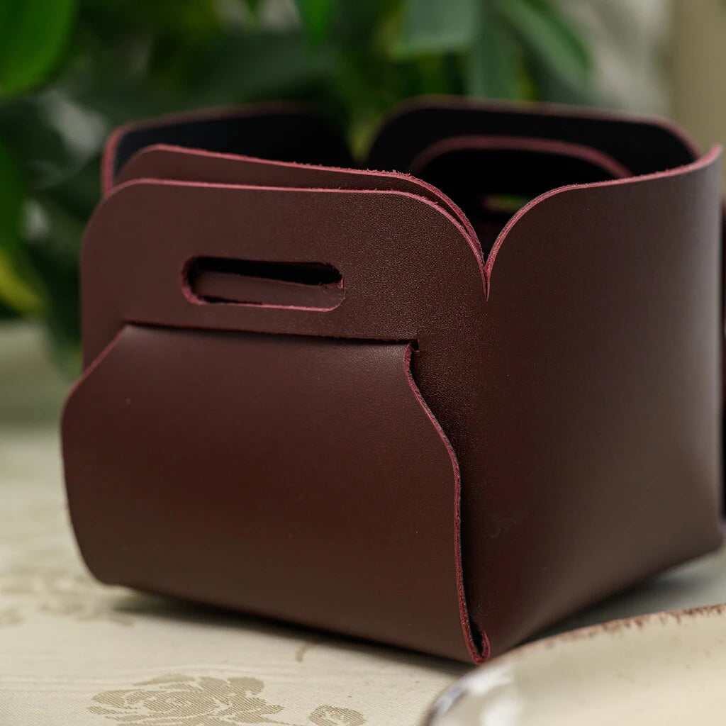 A square leather bread basket in deep burgundy with an interlocking tab design.