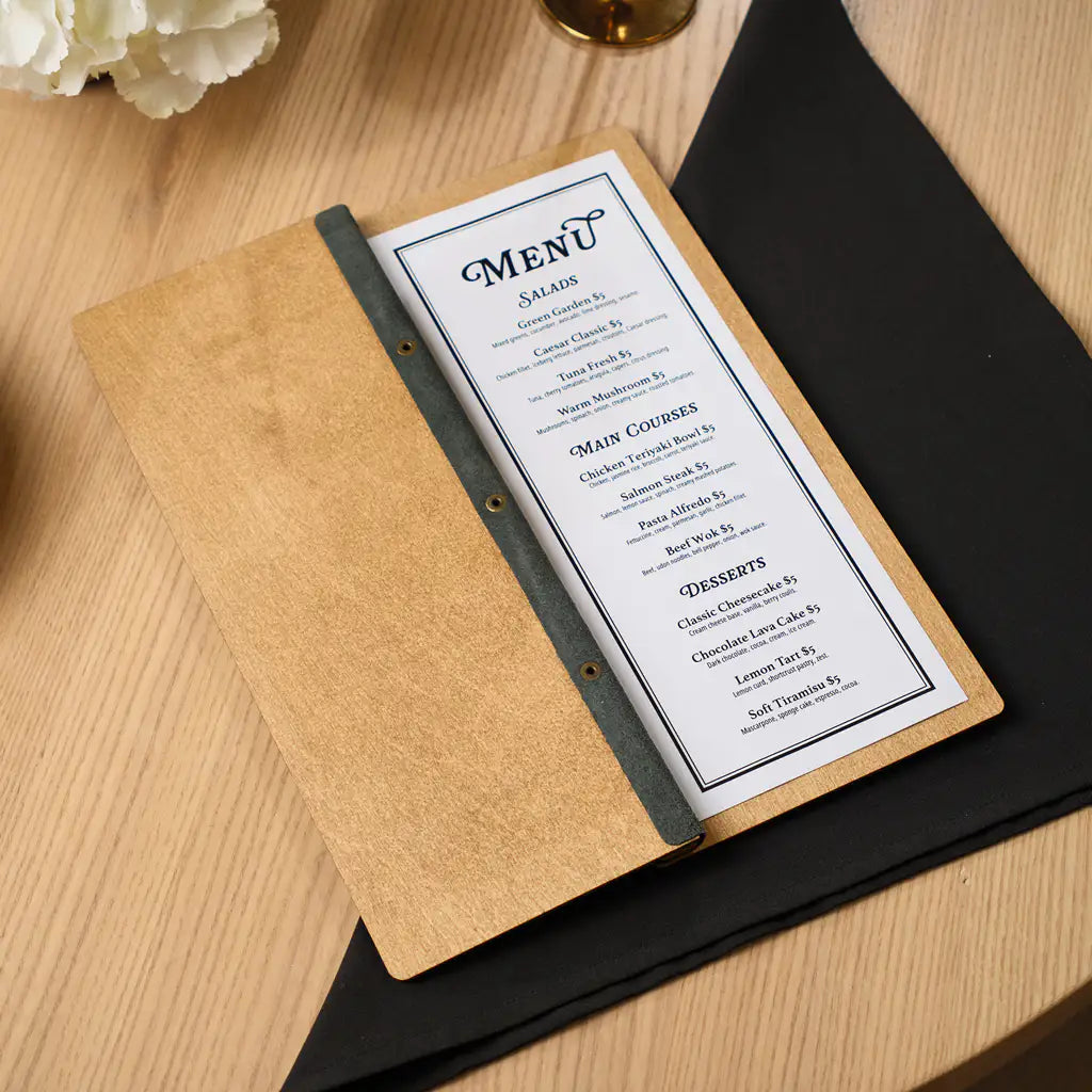 An open view of the oak-colored menu folder resting on a black napkin, featuring a printed menu with sections for Salads, Main Courses, and Desserts