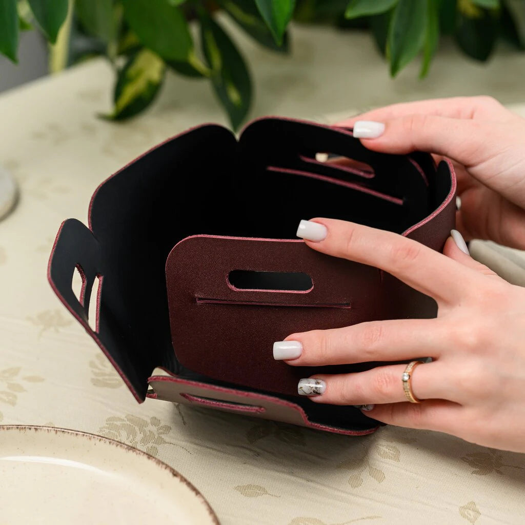 Hands assembling a burgundy leather bread basket by interlocking tabs into slots