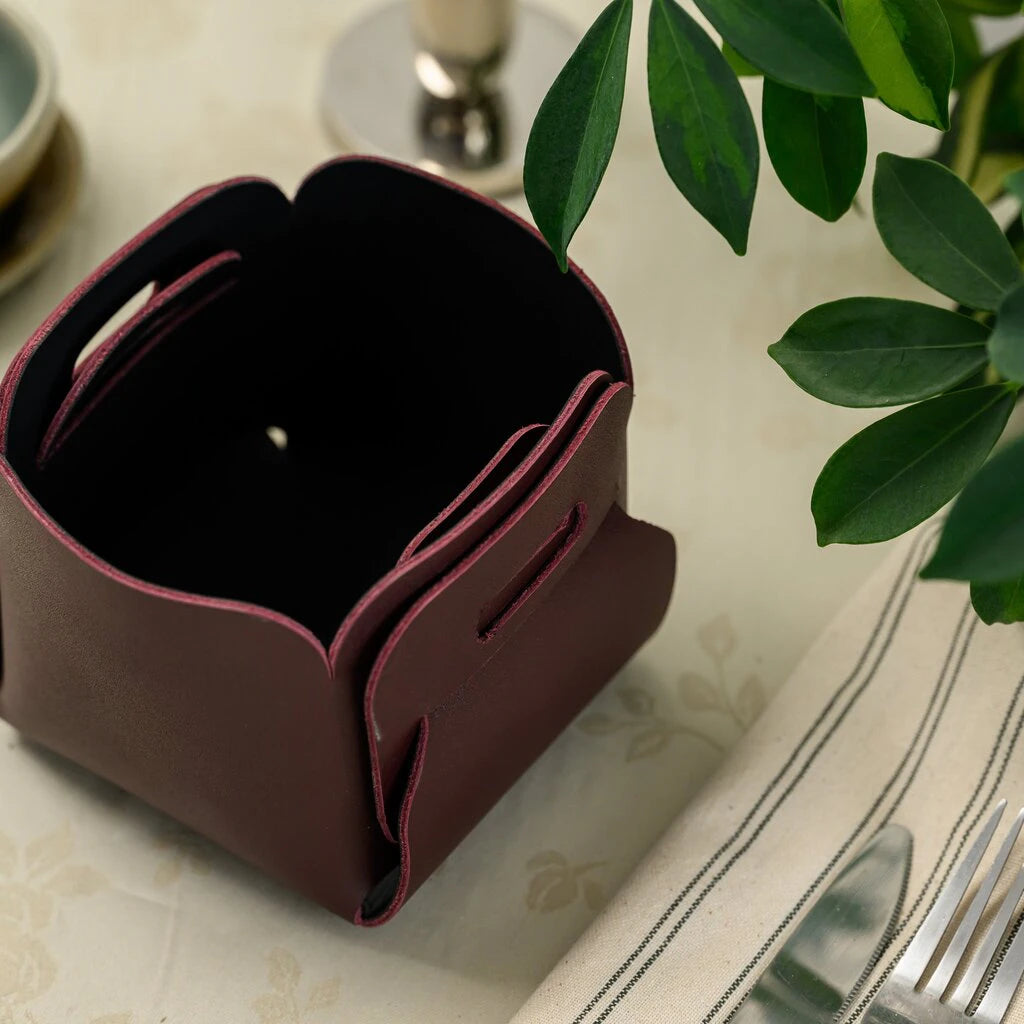 High-angle shot of an empty burgundy leather basket next to a striped napkin and cutlery.