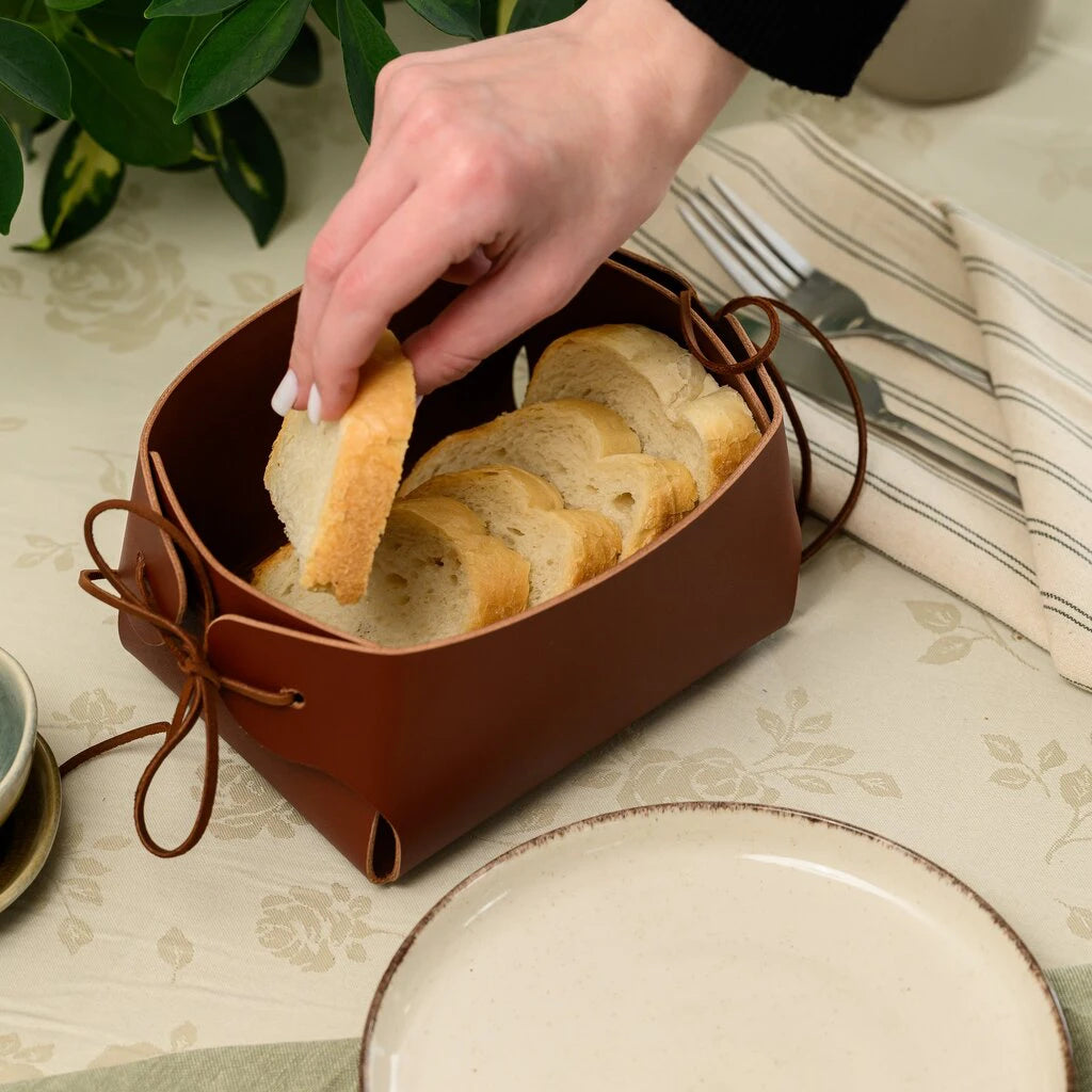 Side view of a deep brown leather bread basket filled with sliced baguette, highlighting the sturdy construction and decorative leather tie fasteners