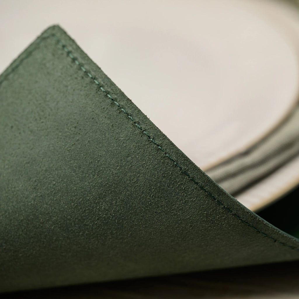 Extreme close-up of the soft suede-like reverse side of a forest green leather placemat, showing detailed stitching and premium non-slip material texture