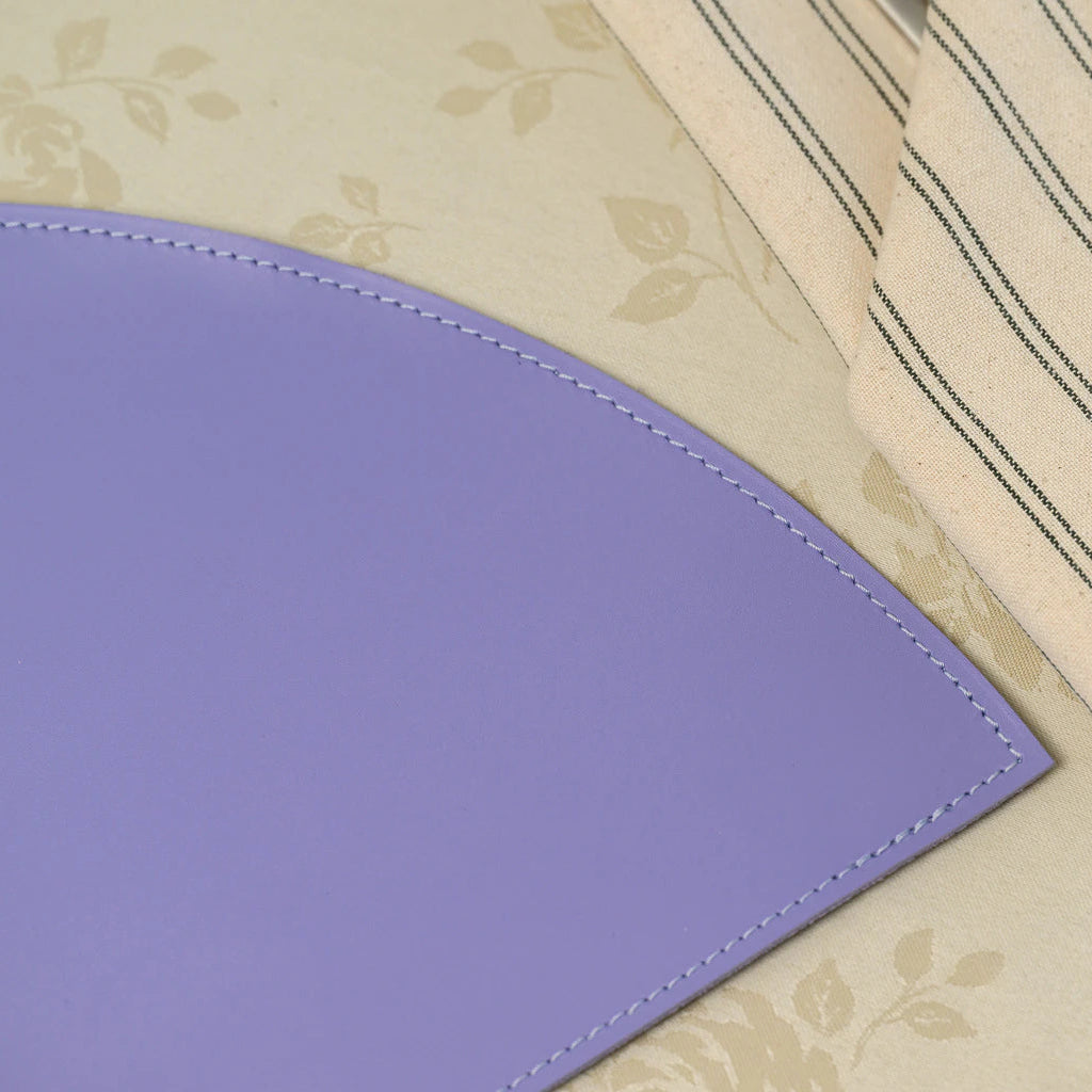 Close-up of the perimeter stitching on a lavender leather placemat, showcasing the precision craftsmanship against a backdrop of a striped linen napkin