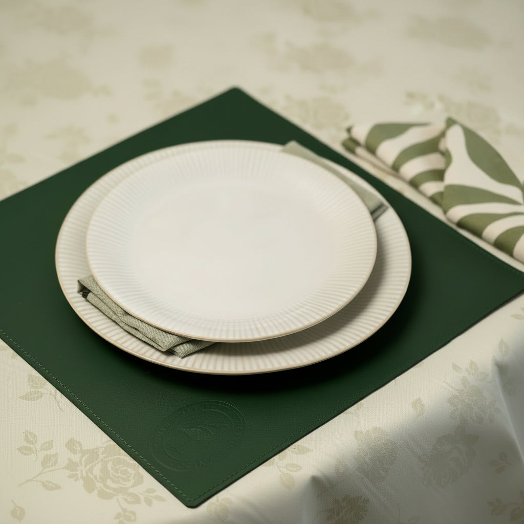 Premium forest green leather placemat with embossed logo and decorative stitching, styled under stacked white ceramic plates on a floral tablecloth