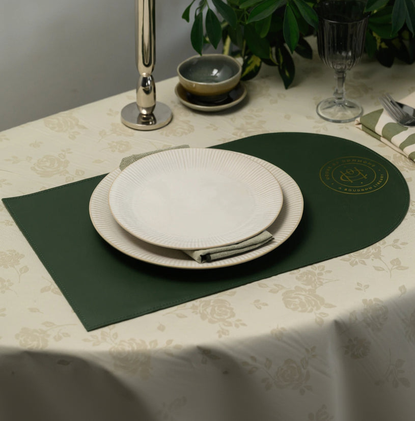 Close-up of a premium forest green leather placemat featuring a detailed gold foil embossed logo that reads "HOUSE OF COMMONS A BOURBON LIBRARY". The image highlights the luxury metallic gold texture and the fine grain of the dark green leather