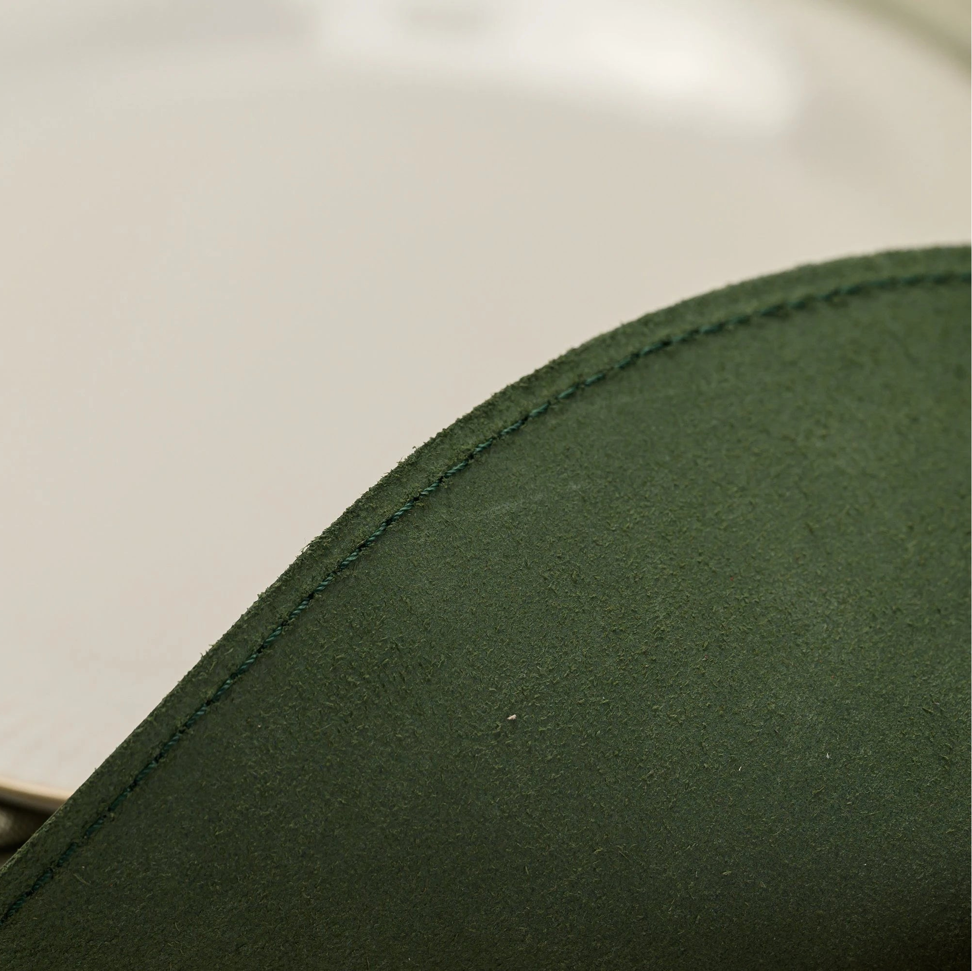 Forest green D-shaped leather placemat with a straight edge and a large curved side. Features a prominent gold foil embossed logo "HOUSE OF COMMONS A BOURBON LIBRARY" in the center. Styled on a cream floral tablecloth with stacked white ribbed ceramic plates.