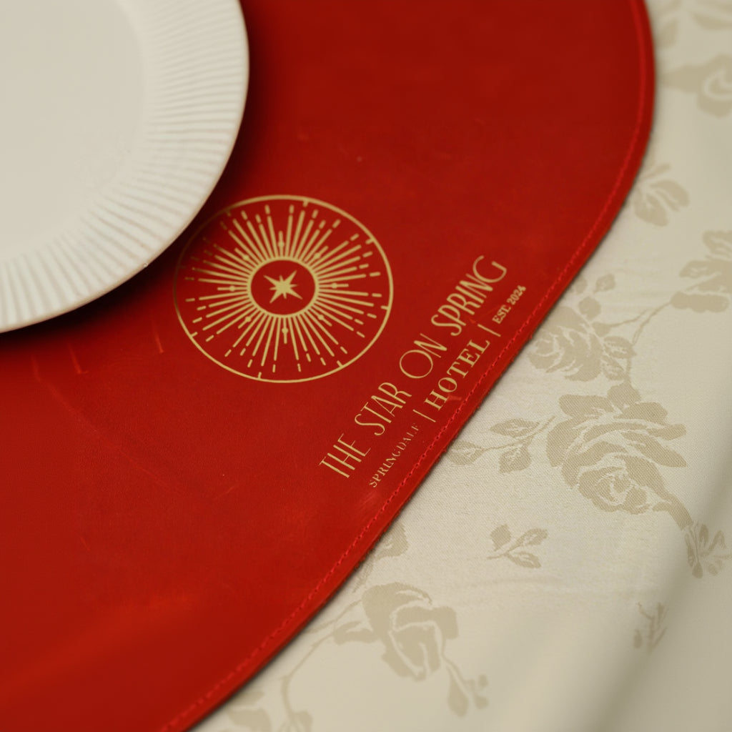 Oval red leather placemat with a luxury gold foil 'THE STAR ON SPRING HOTEL' logo, featuring decorative perimeter stitching and a white ribbed plate