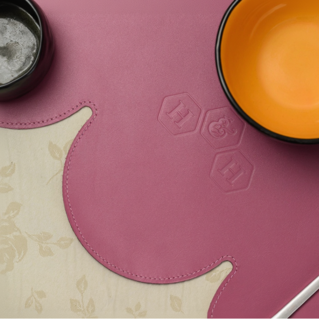 Magenta leather placemat with an embossed hexagonal logo and a black and orange bowl on top.