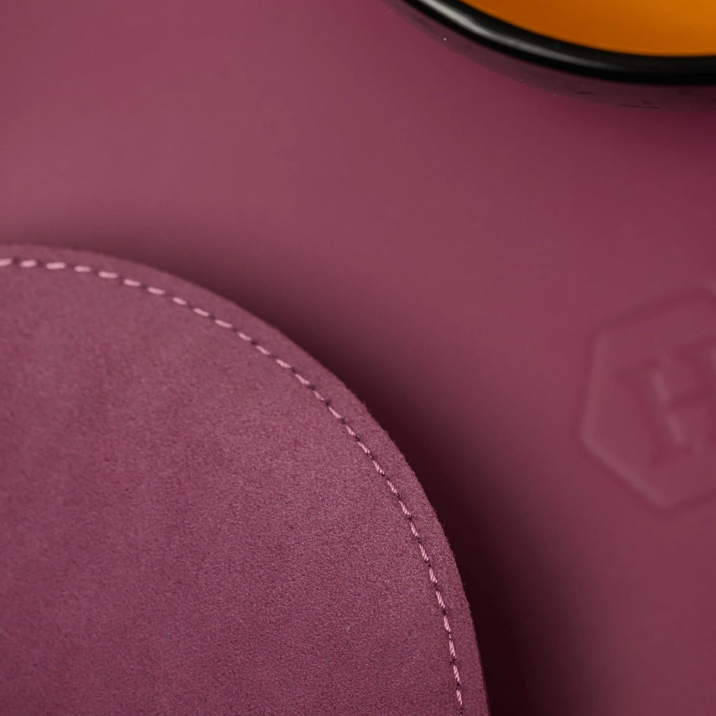 A macro shot showing the premium textures of a magenta dining set: a smooth leather placemat with a hexagonal embossed logo and a circular suede coaster with neat perimeter stitching.