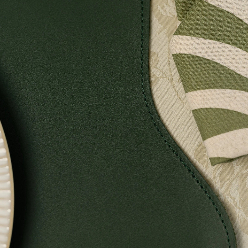 Close-up detail of a dark green faux leather table mat with a curved decorative edge, highlighting the smooth matte finish and precision stitching