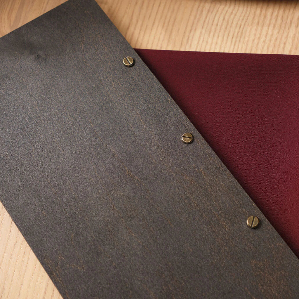 A detailed shot of the back cover's binding, showing three antique brass slotted screws set into the dark wenge wood against a burgundy background.