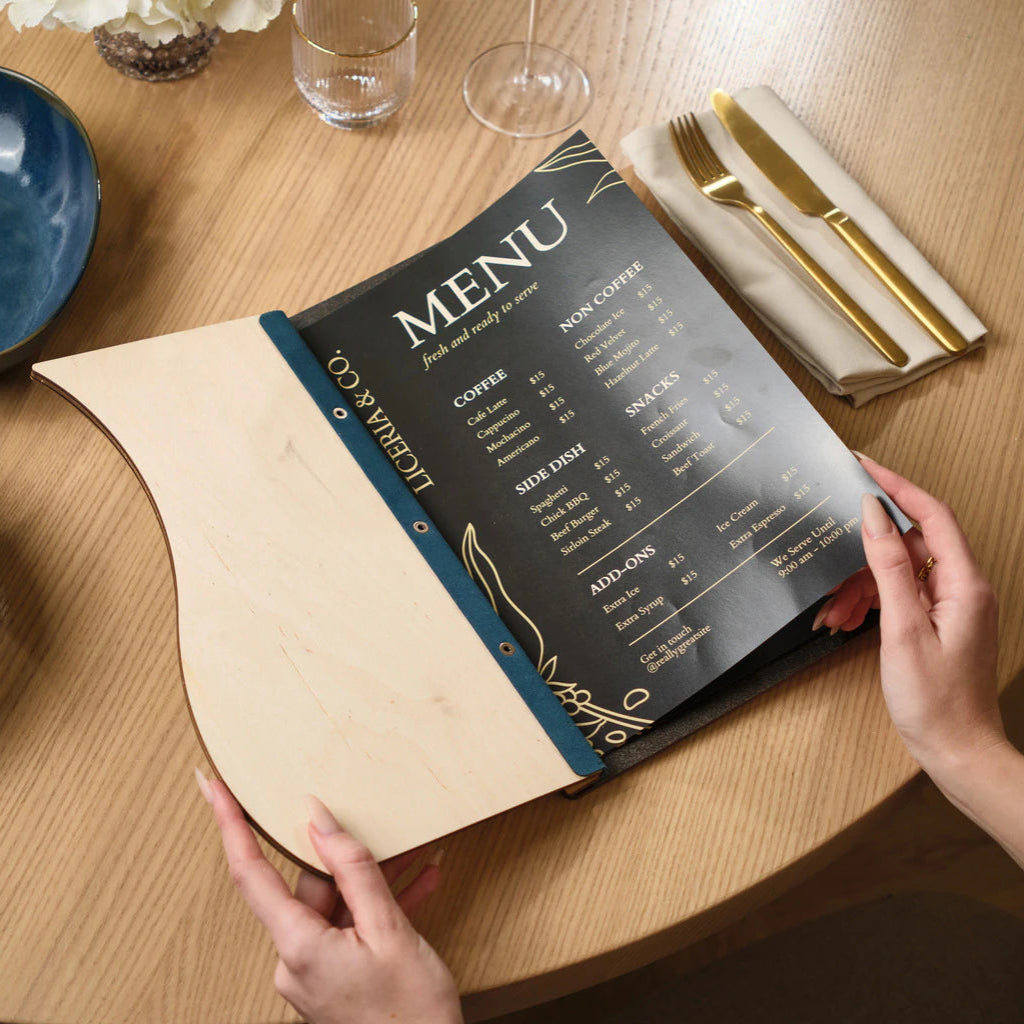Top-down view of an open custom wooden menu on a restaurant table, showing the contrast between the light wood interior and the dark menu card