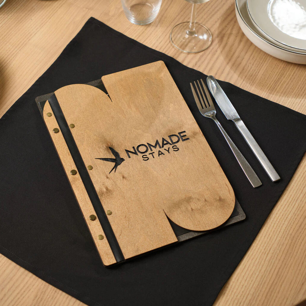 Wooden menu folder with a unique custom cutout and "NOMADE STAYS" logo engraving on a set table