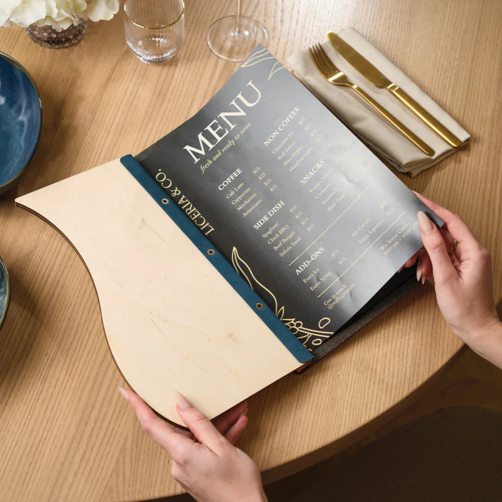 A person holding open a wavy wood menu board to display a black "Liceria & Co." menu card, showcasing the inner Ivory wood finish and blue spine