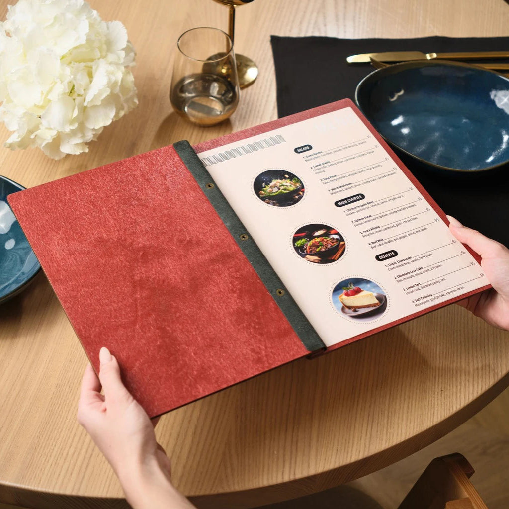Internal view of an open red wooden menu folder held by a customer, showcasing high-quality printed inserts for salads, main courses, and desserts. The handcrafted wood menu cover features a secure black leather hinge and professional bronze bolt binding