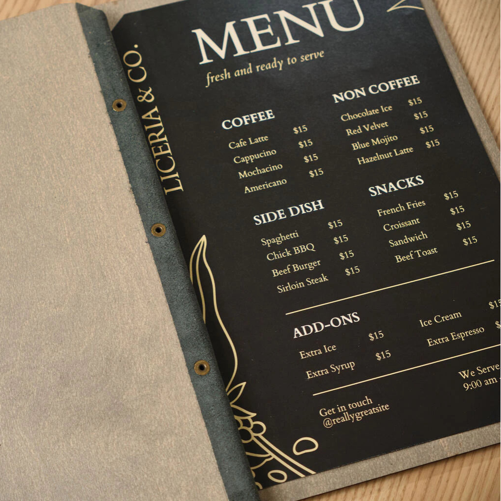 Detailed shot of an open handcrafted wooden menu featuring a dark gray leather-style spine secured by brass rivets, highlighting a modern "Liceria & Co." menu design