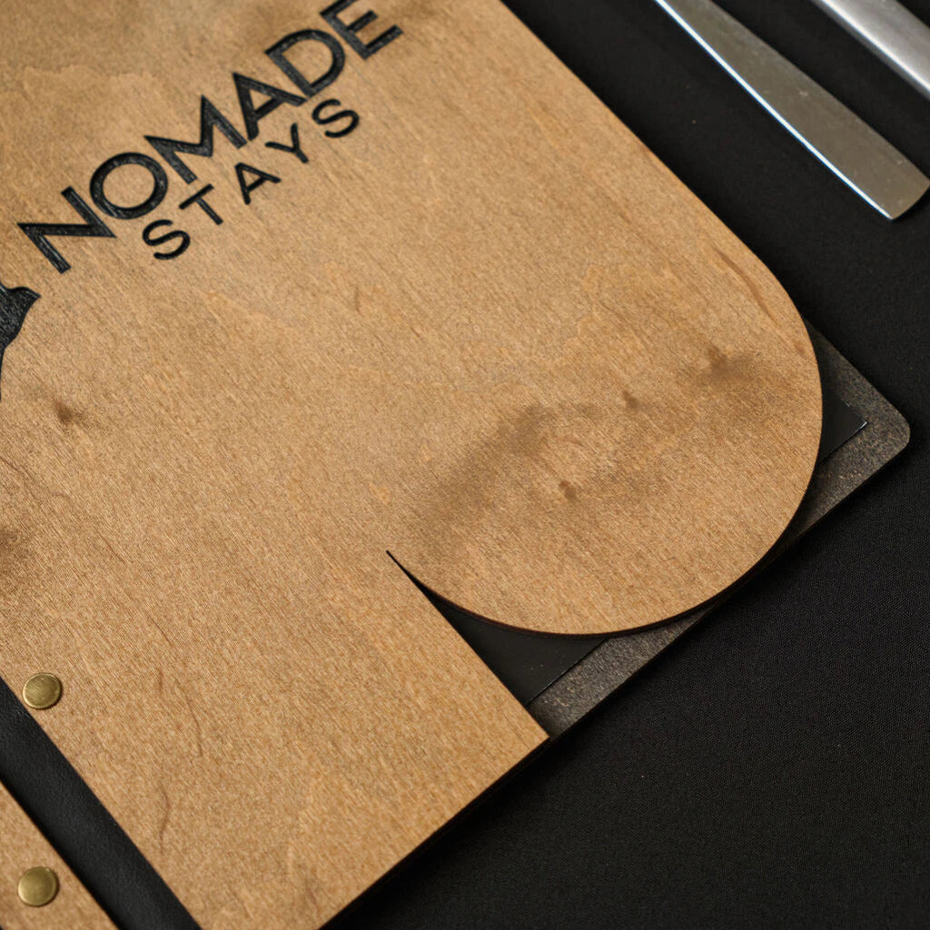Macro photo of a natural oak wooden folder, highlighting the wood grain texture and the detailed "NOMADE STAYS" logo engraving