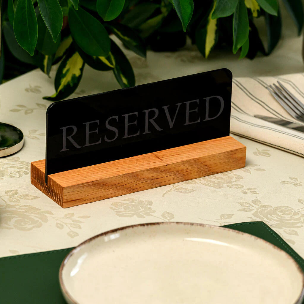 Macro view of a stylish black and wood restaurant reservation sign, highlighting the smooth matte finish and natural wood grain