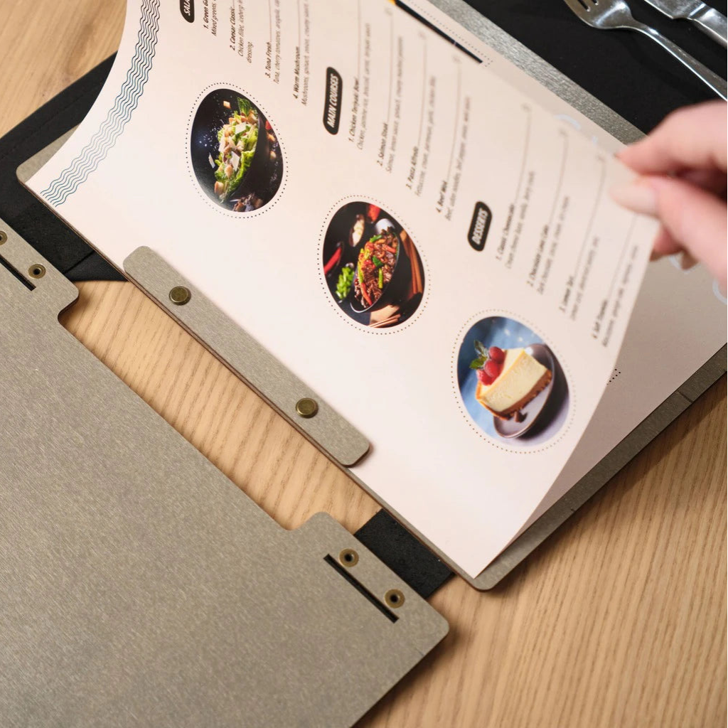 Detailed view of the handcrafted interior of a premium wood menu holder in a modern grey finish. The image highlights the secure bronze hardware and flexible leather spine that allows for easy page replacement in a restaurant setting