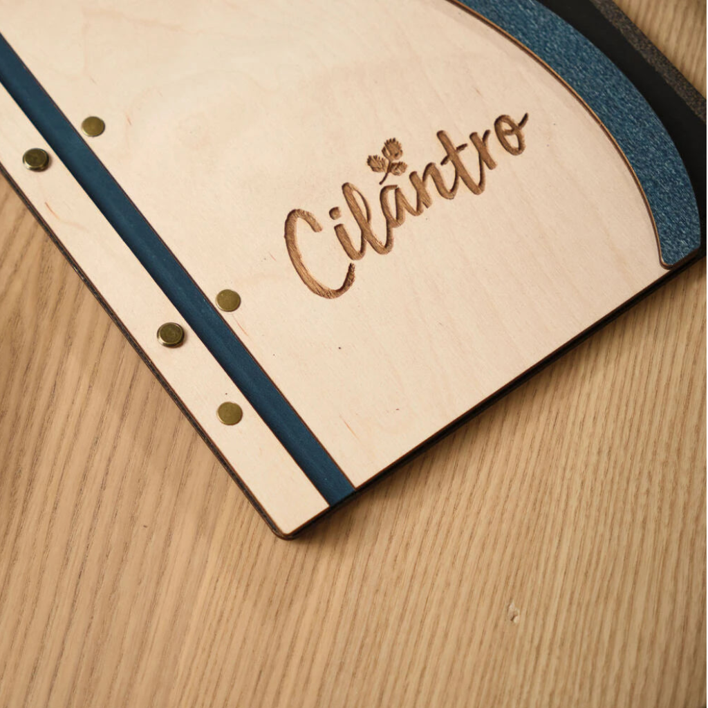 Detailed view of the handcrafted ivory wooden menu surface, showing the precise laser-cut logo and professional antique brass screw posts for a secure bind