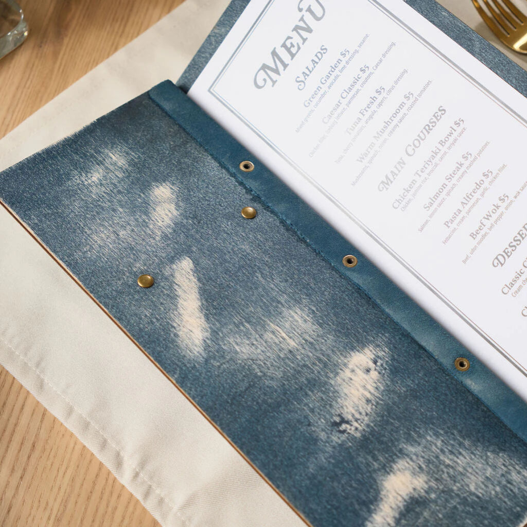 An angled close-up emphasizing the handcrafted look of the blue distressed wood and the leather binding used to secure the printed menu pages.