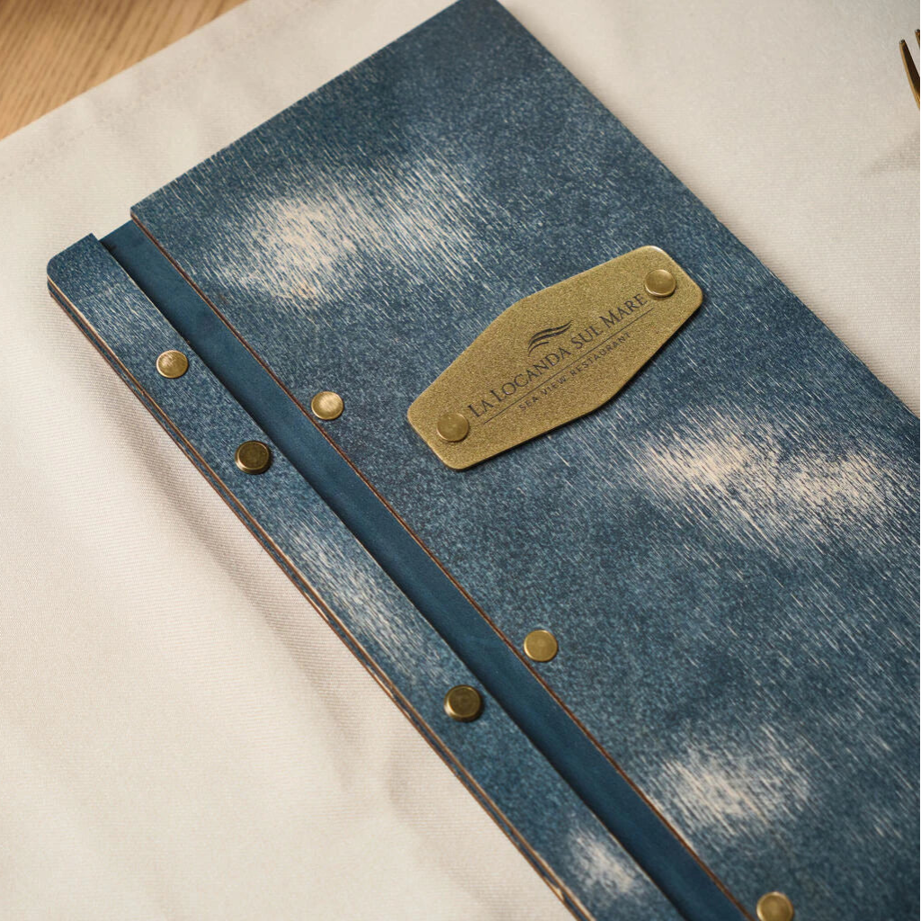 Detailed shot of a handcrafted blue wooden menu with vintage brass rivets and an engraved gold nameplate