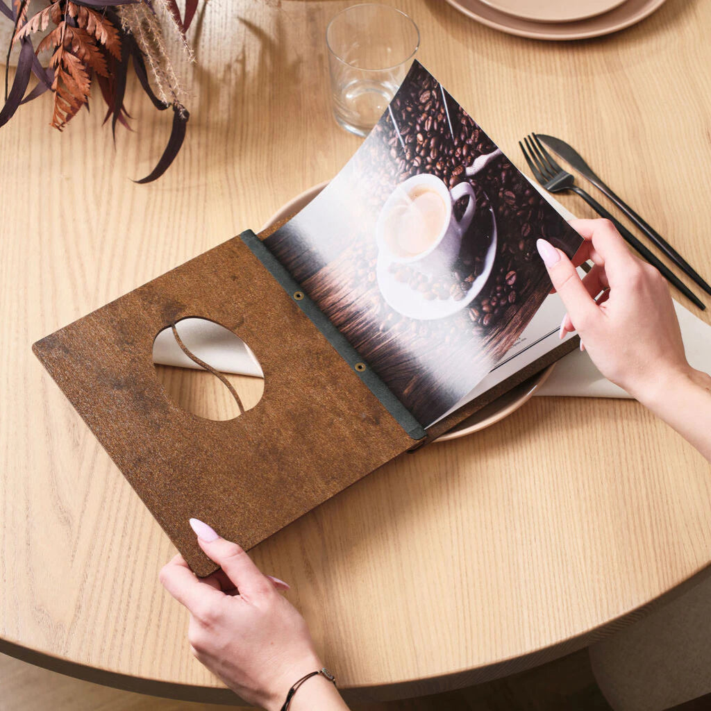 An open wooden menu featuring a coffee bean cutout on the cover and a high-quality photo of a latte on the inner page.