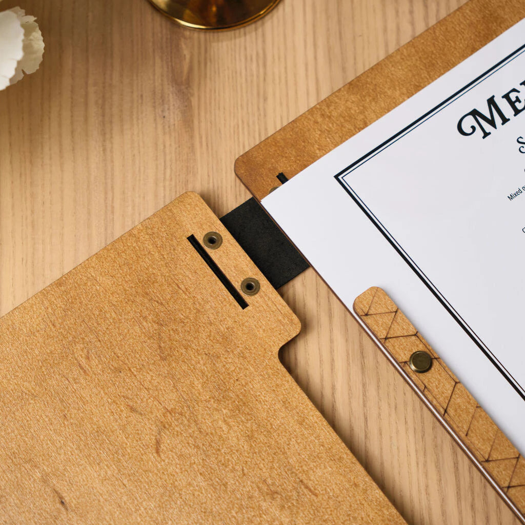 English: Close-up of the upper part of a wooden menu board, showing the combination of light oak, a black leather spine, and brass fasteners