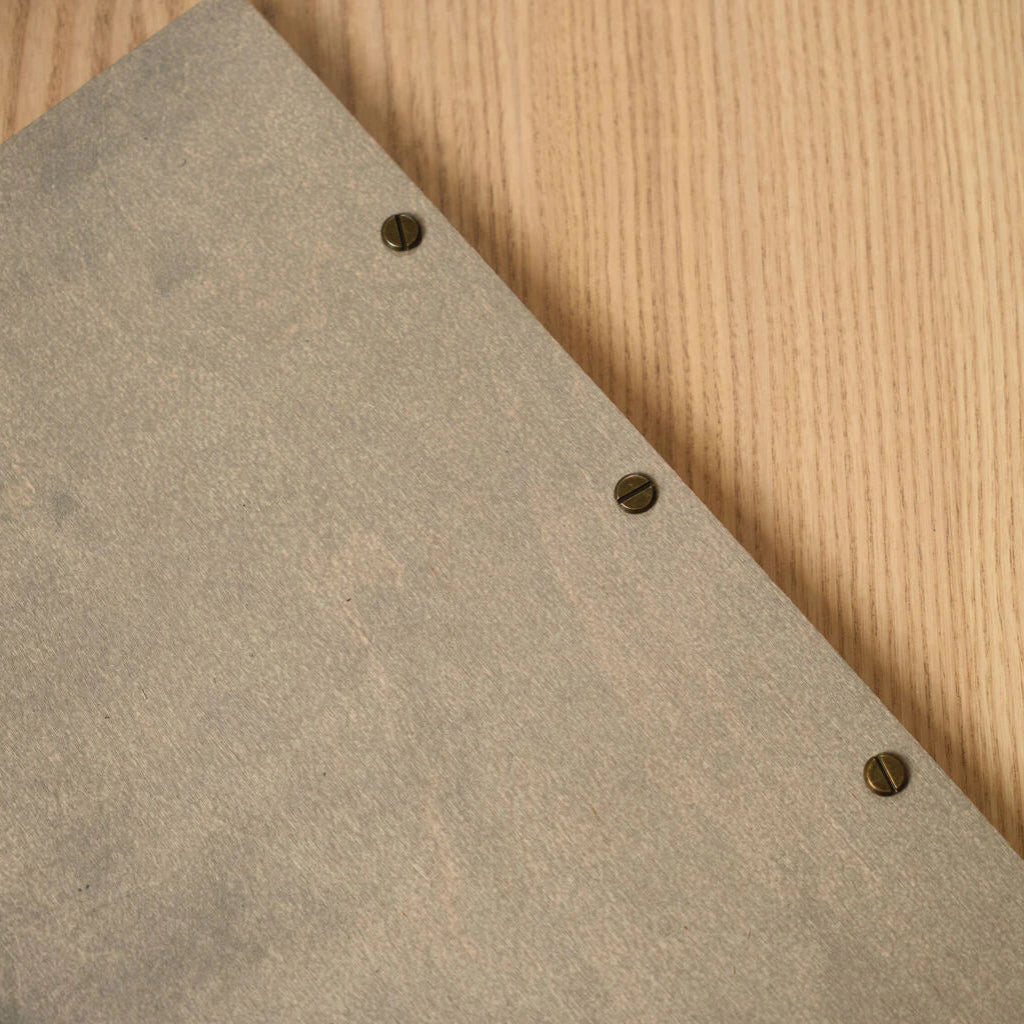 Macro close-up of antique bronze screw hardware securing a custom gray wood menu folder, highlighting the grain of the wood and metallic detail