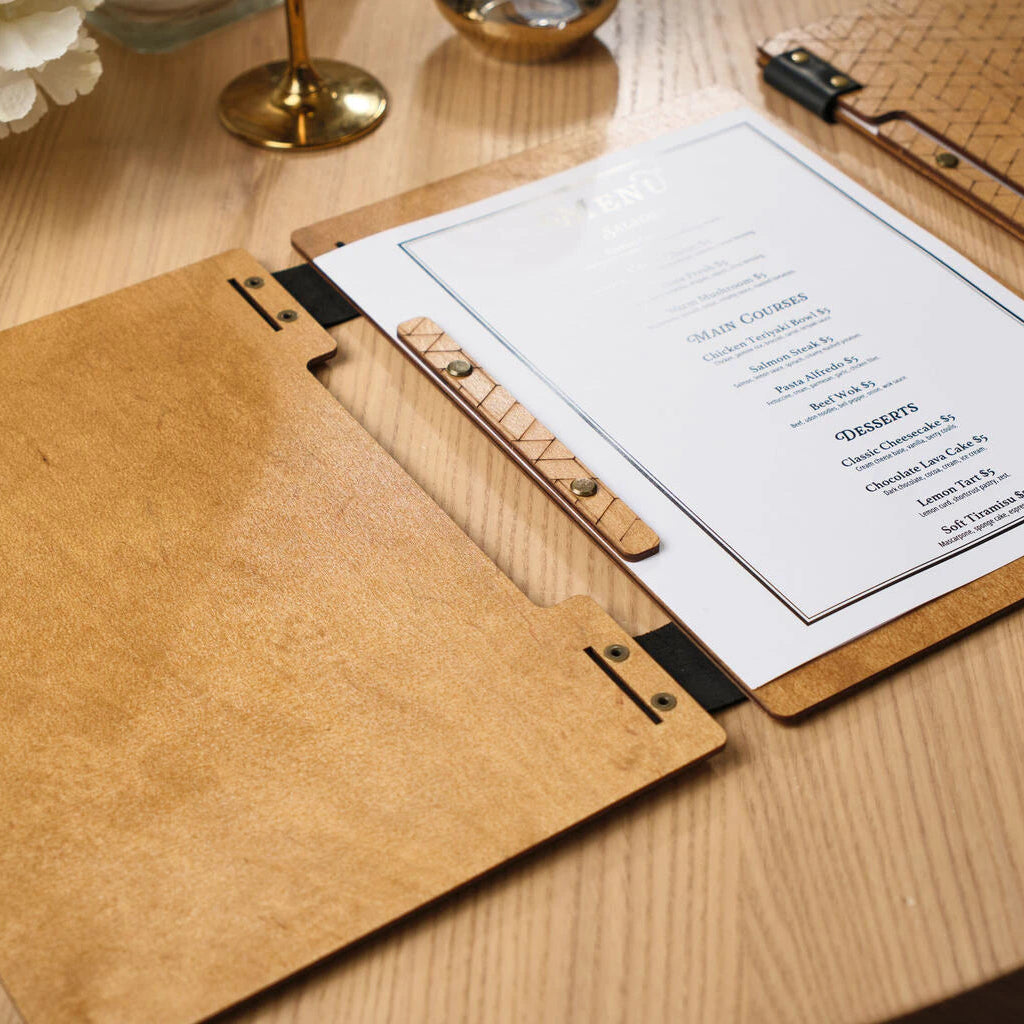 Perspective view of an open wooden menu board with a printed menu, lying on a wooden table next to a wine glass