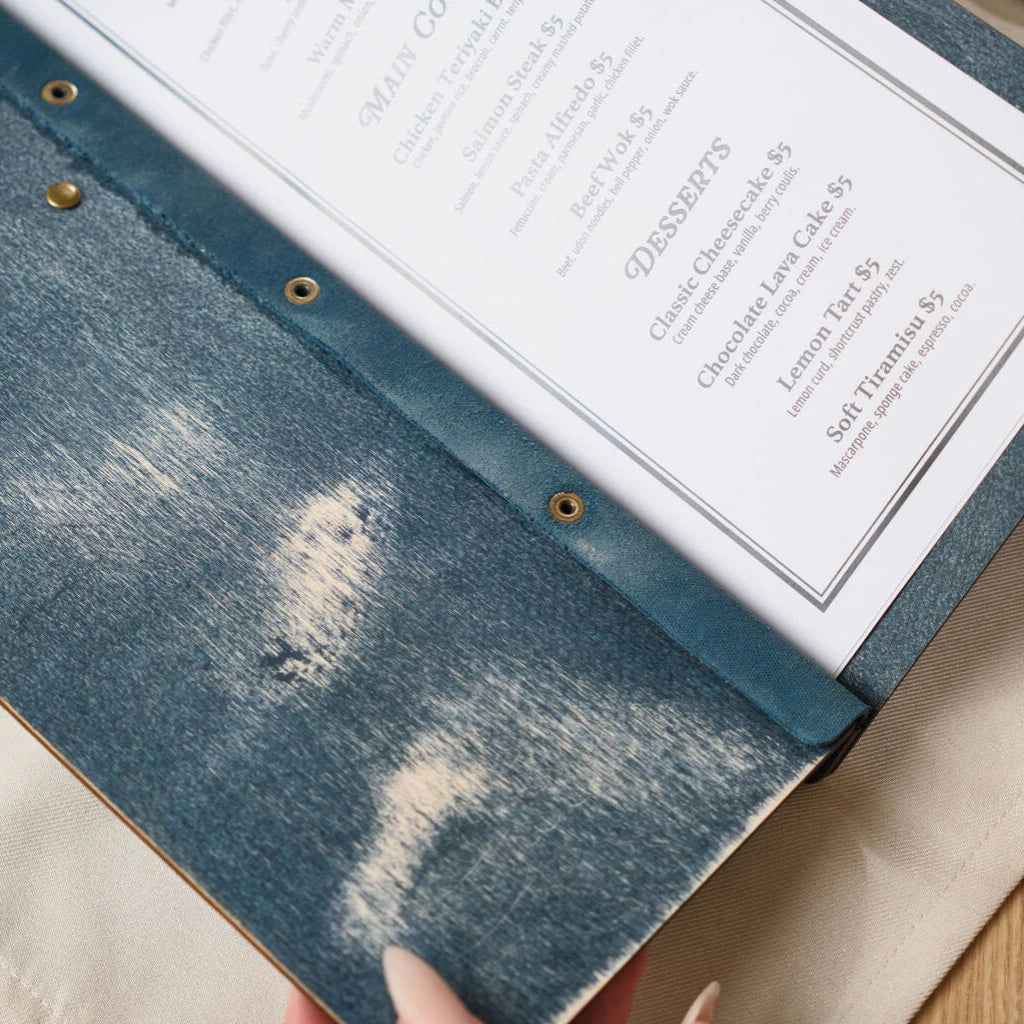 A detailed view of the lower half of the opened blue wooden menu, showing the natural wood grain showing through the blue stain and the reinforced metal eyelets along the spine.