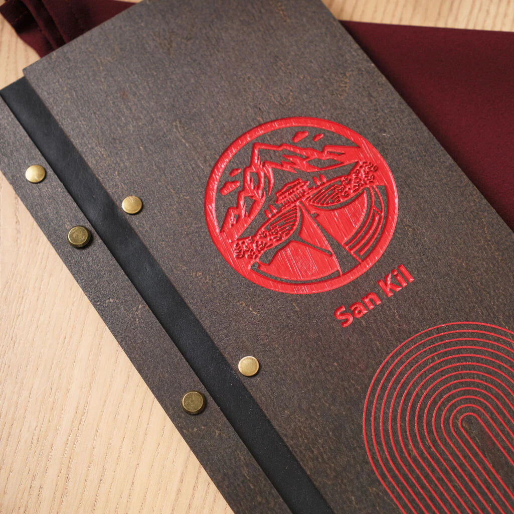 A detailed shot of the menu folder, showcasing the contrast between the red mountain logo and the black leather binding strip secured with antique brass rivets.
