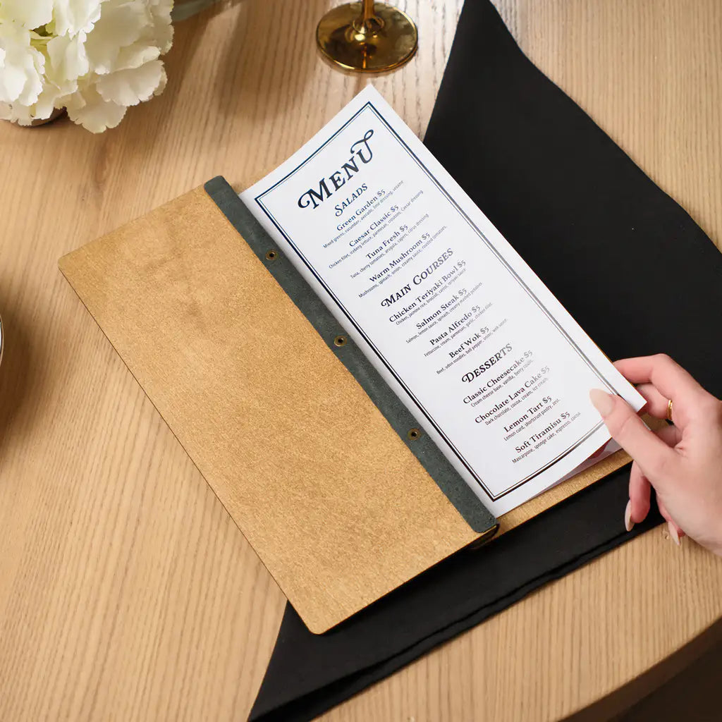 A top-down perspective of the open wooden menu resting on a black napkin, highlighting the clear layout of the "Salads," "Main Courses," and "Desserts" sections on the white paper insert.