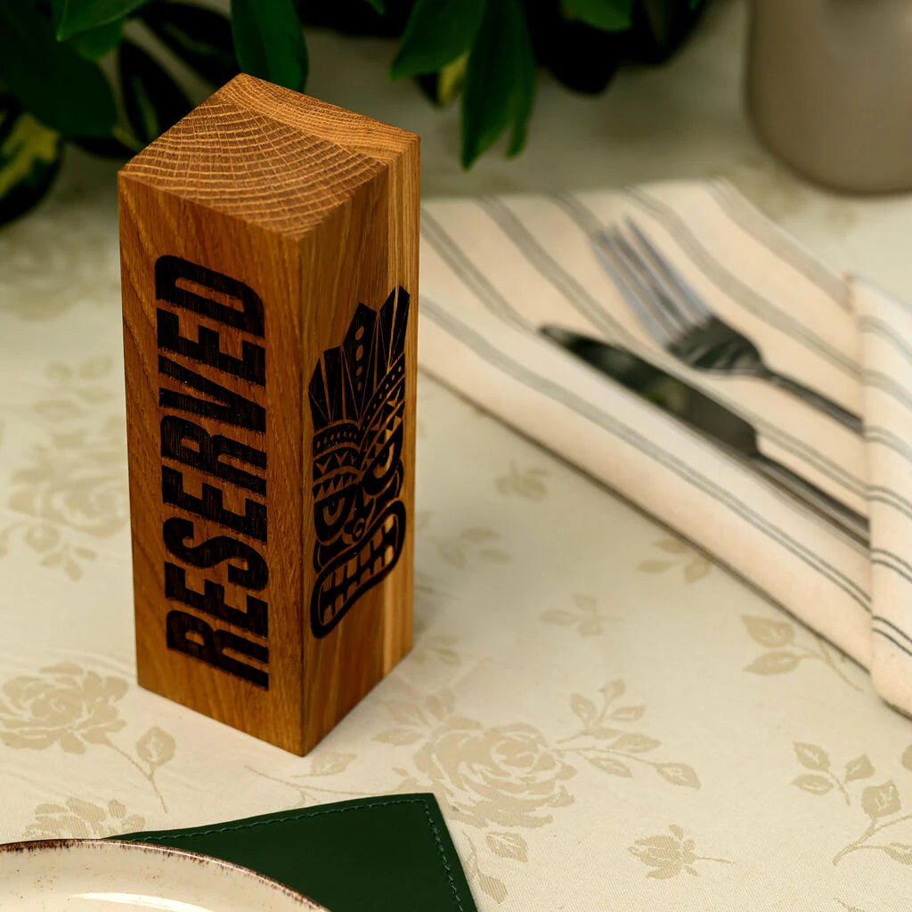 A stylish wooden reservation block handcrafted from premium oak. The warm tones of the wood and the unique Tiki-themed laser engraving add a tropical yet sophisticated touch to the restaurant's table setting. The vertical design ensures the sign is easily visible to guests and staff