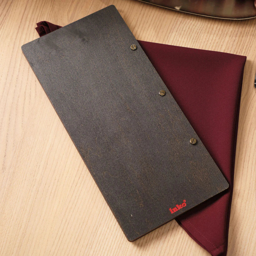 The back cover of the menu folder, showing the smooth wenge wood texture, the brass binding screws, and a small red "inko" brand logo in the bottom corner.
