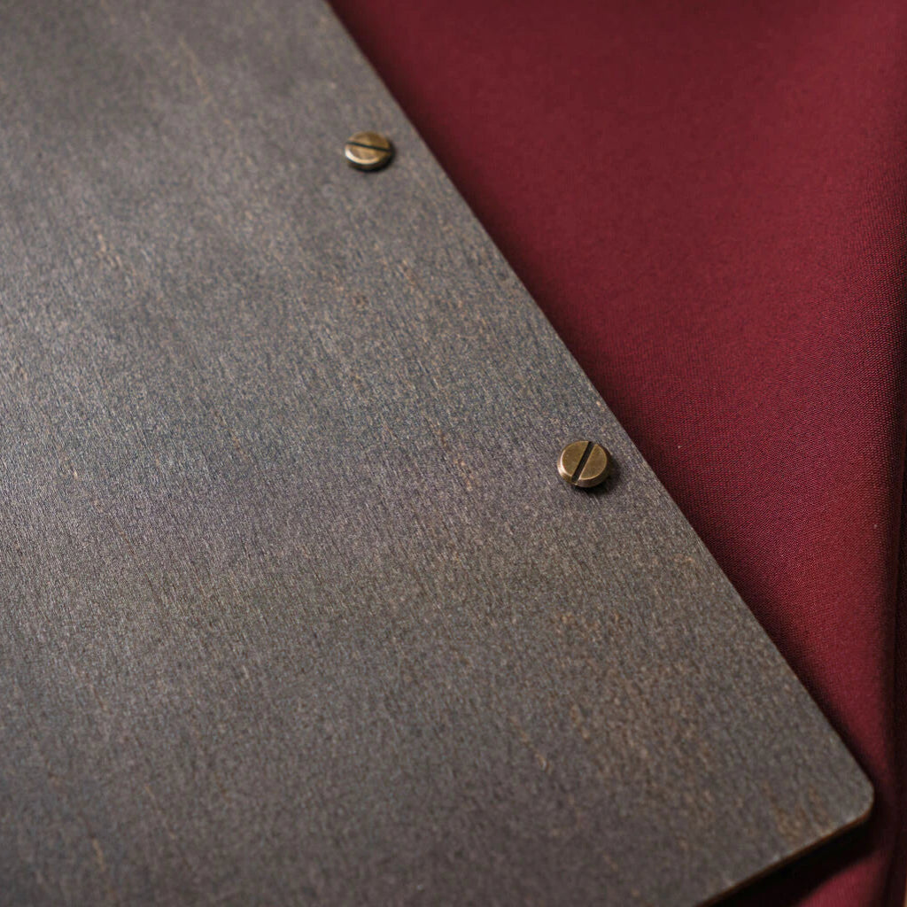A close-up perspective of two brass binding screws on the wenge wood cover, highlighting the natural grain and dark stain of the material.