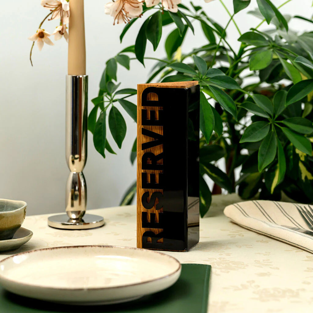 Premium restaurant table setting featuring a modern handcrafted wooden reservation sign with a sleek black acrylic finish and bold lettering