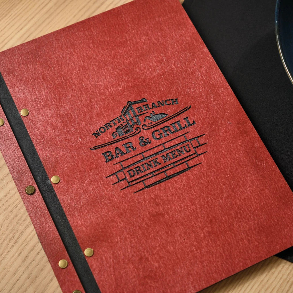 Close-up of a red wooden menu folder with custom black laser engraving for North Branch Bar & Grill. Shows the premium textured wood finish, black leather spine, and secure bronze bolt binding