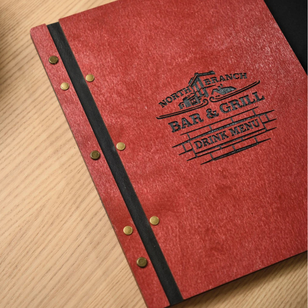 Close-up of a red wooden drink menu folder with a custom black logo for North Branch Bar & Grill. This handcrafted wood menu cover features a flexible black leather hinge and professional bronze bolt binding