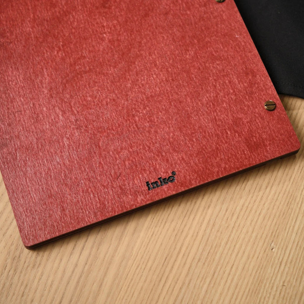 Detailed close-up of the back of a red wooden menu folder featuring a small engraved "inko" logo. This handcrafted wood menu cover highlights the premium grain texture and professional bronze screw-post binding