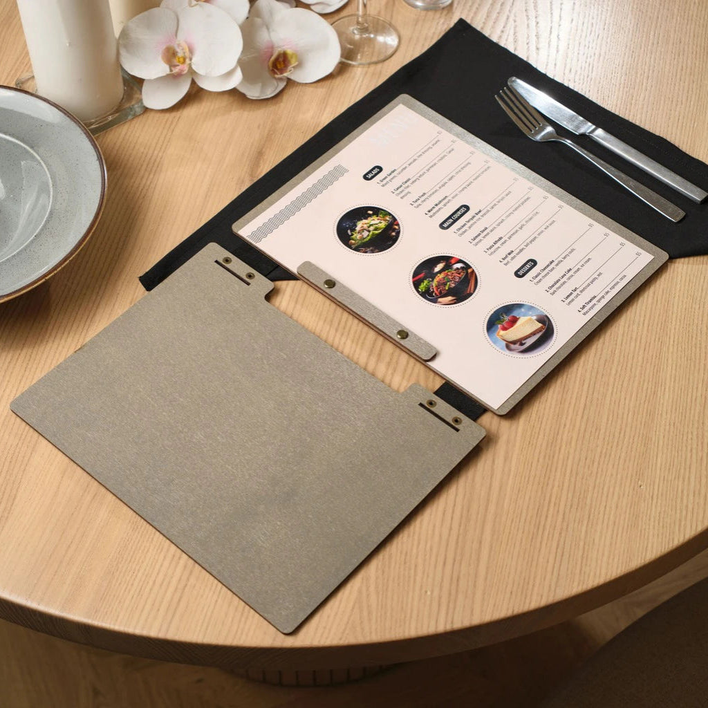 Internal view of an open grey wooden menu folder showcasing high-quality printed inserts for salads, main courses, and desserts. This handcrafted wood menu cover features a unique black leather strap binding and professional bronze bolt hardware on a modern restaurant table