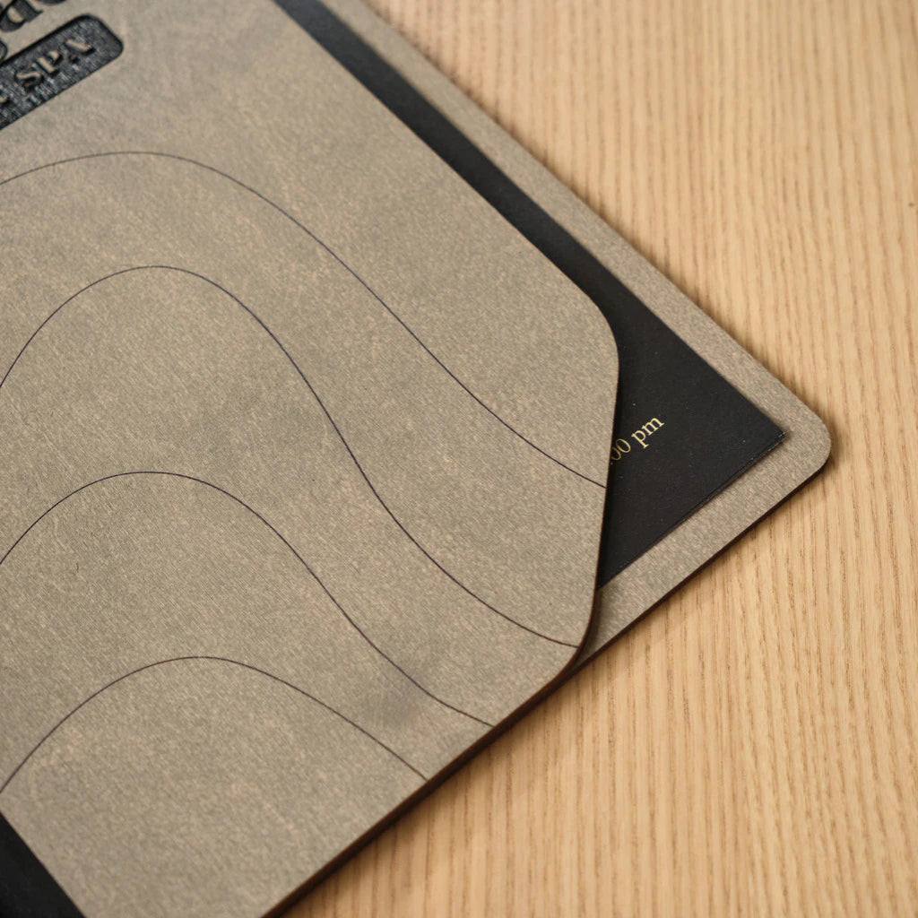 Detail view of handcrafted gray wood texture and elegant brass hardware on a spa menu folder next to stainless steel cutlery