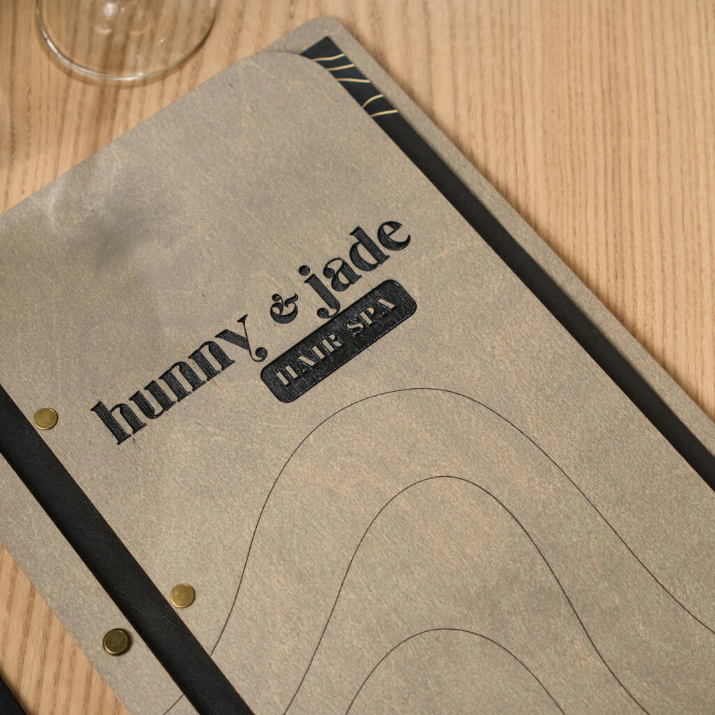 Close-up of a high-quality engraved logo and spa branding on a gray wooden menu holder with premium brass screw finishes
