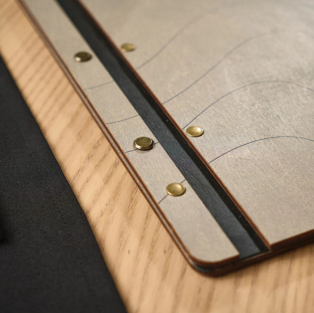 Close-up of brass decorative bolts securing a leather spine to a wooden menu board, showing professional craftsmanship