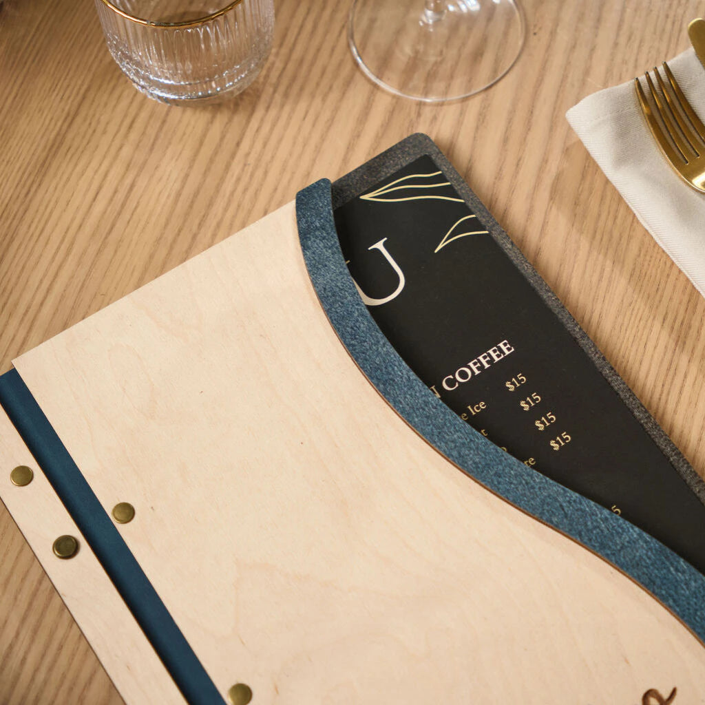 Top-down detail of the unique curved edge design on a wooden menu board, revealing a black printed menu card underneath a Jeans blue textured frame