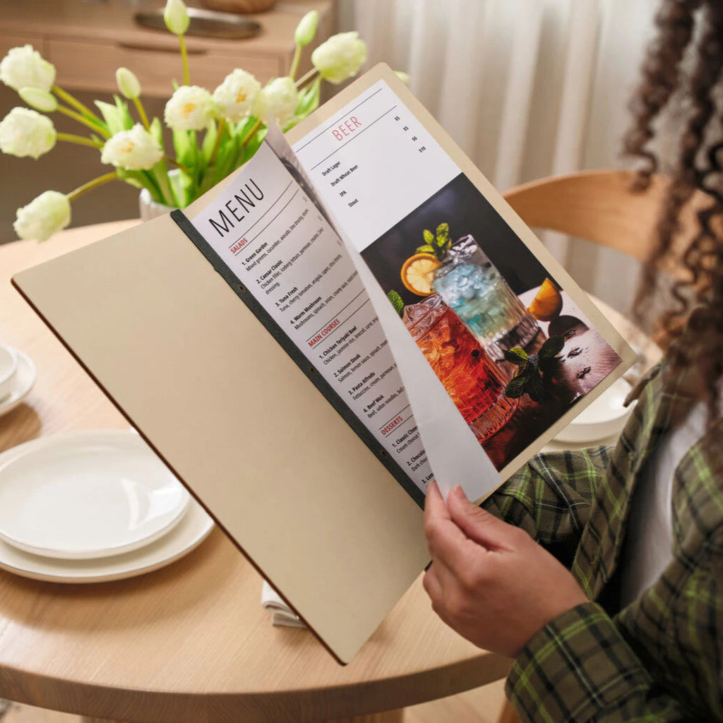 Woman reading open wooden menu holder with printed menu pages showing food and cocktail photos