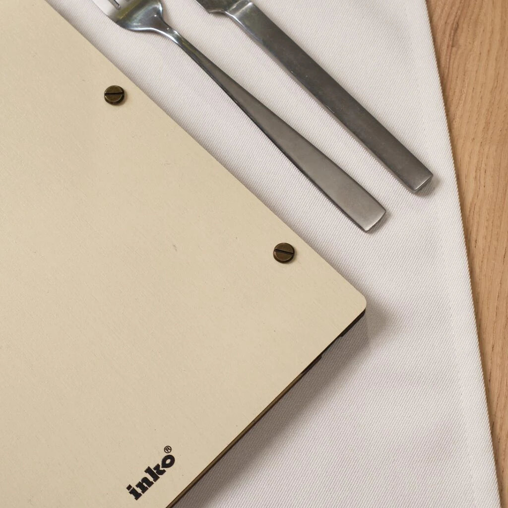 Close-up of Inko wooden menu cover with brass screws and fork and knife on white linen napkin