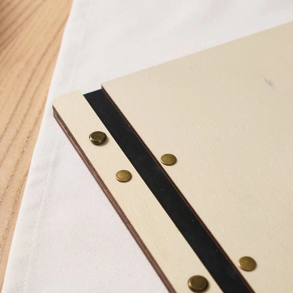Close-up of wooden menu cover spine with black elastic band and brass rivets on white linen